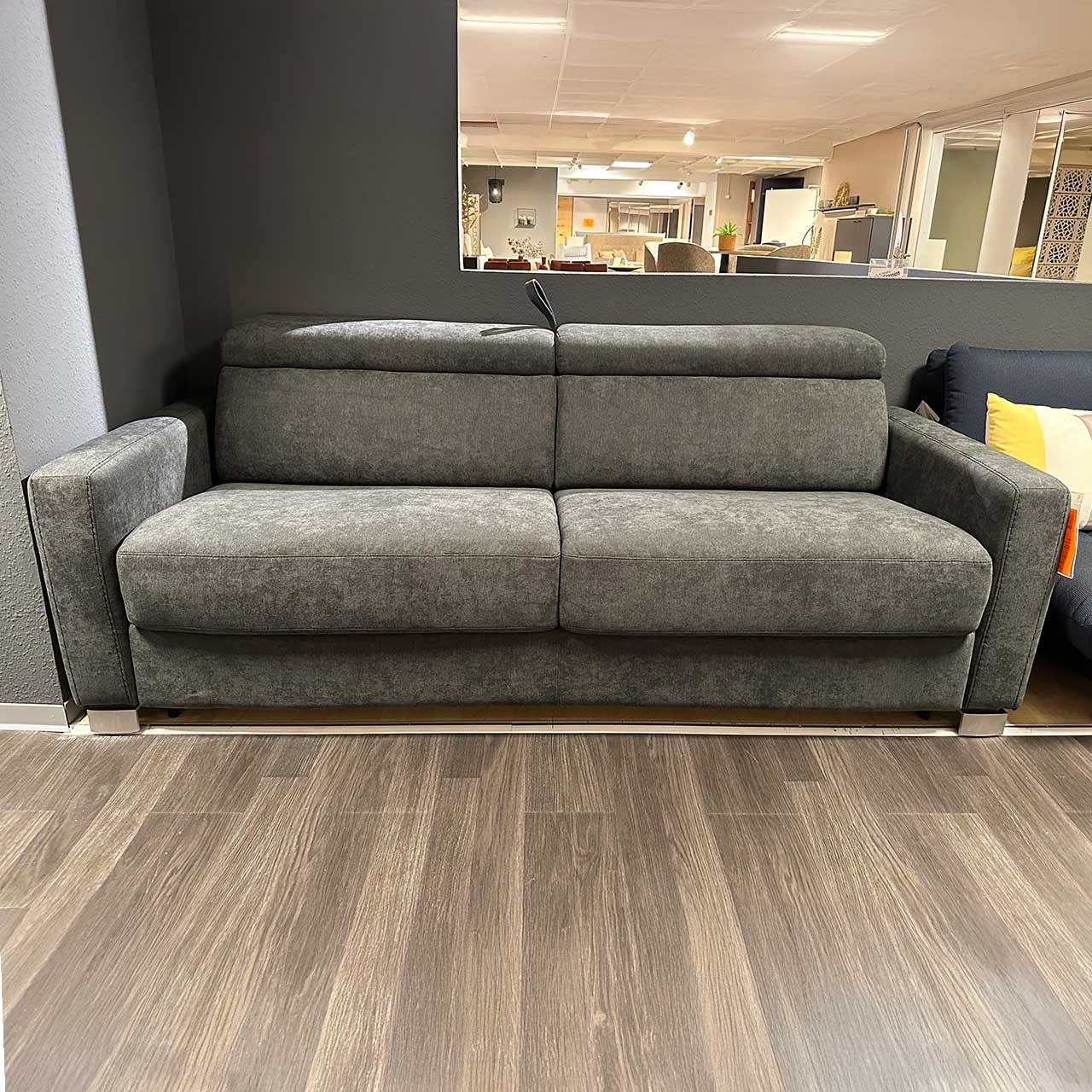Graues stoffbezogenes Zweisitzer-Sofa mit abgeklappten Kopfstützen. Die Schlaufe zum Umwandeln in ein Schlafsofa ist oben zwischen den Lehnen sichtbar.