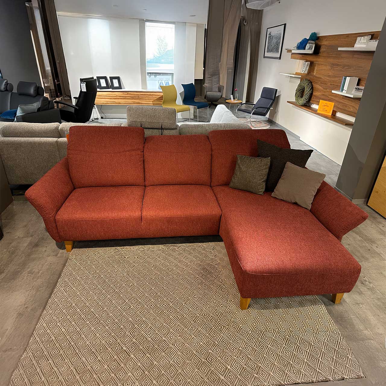 Activineo - Sofa Belami Lugo Ecksofa in dezent rotem Stoff, links zwei Sitzelemente, rechts ein Liegeelement. Abgerundete gepolsterte Lehnen auf beiden Seiten. Holzfüße in hellem Holz.