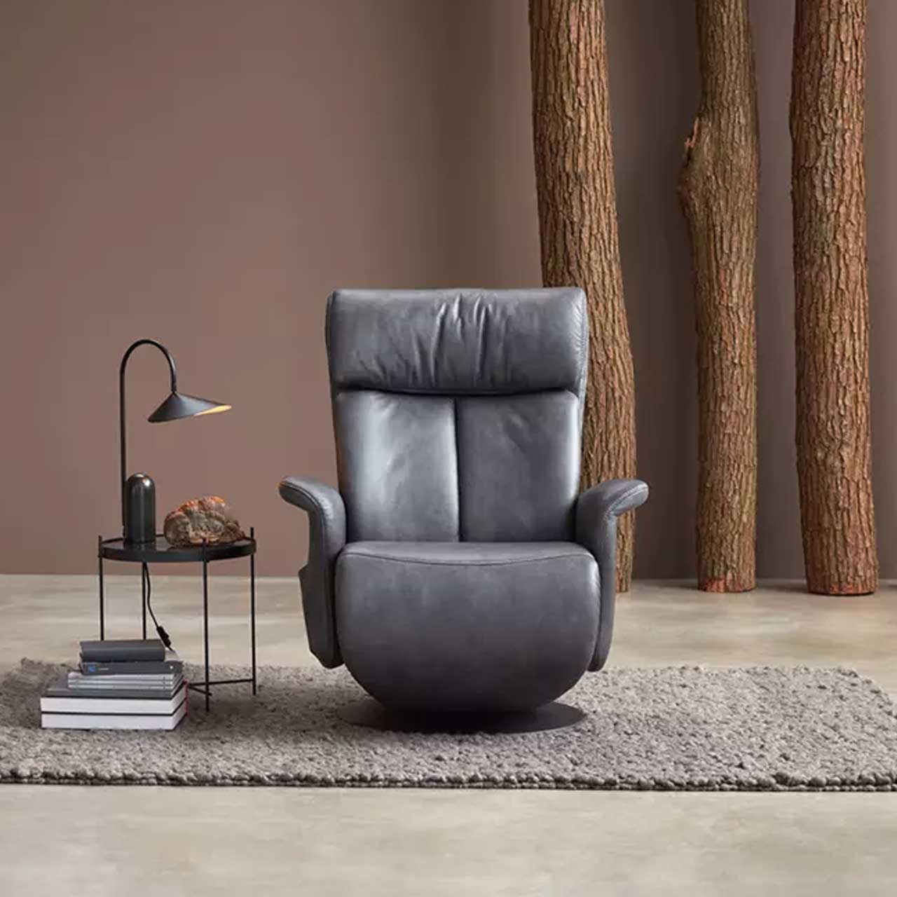 MH_Wohnzimmer_Sessel_Quadratbild Ambientebild mit Ledersessel und dekorativen Baumstämmen im Hintergrund. Coffeetable daneben.