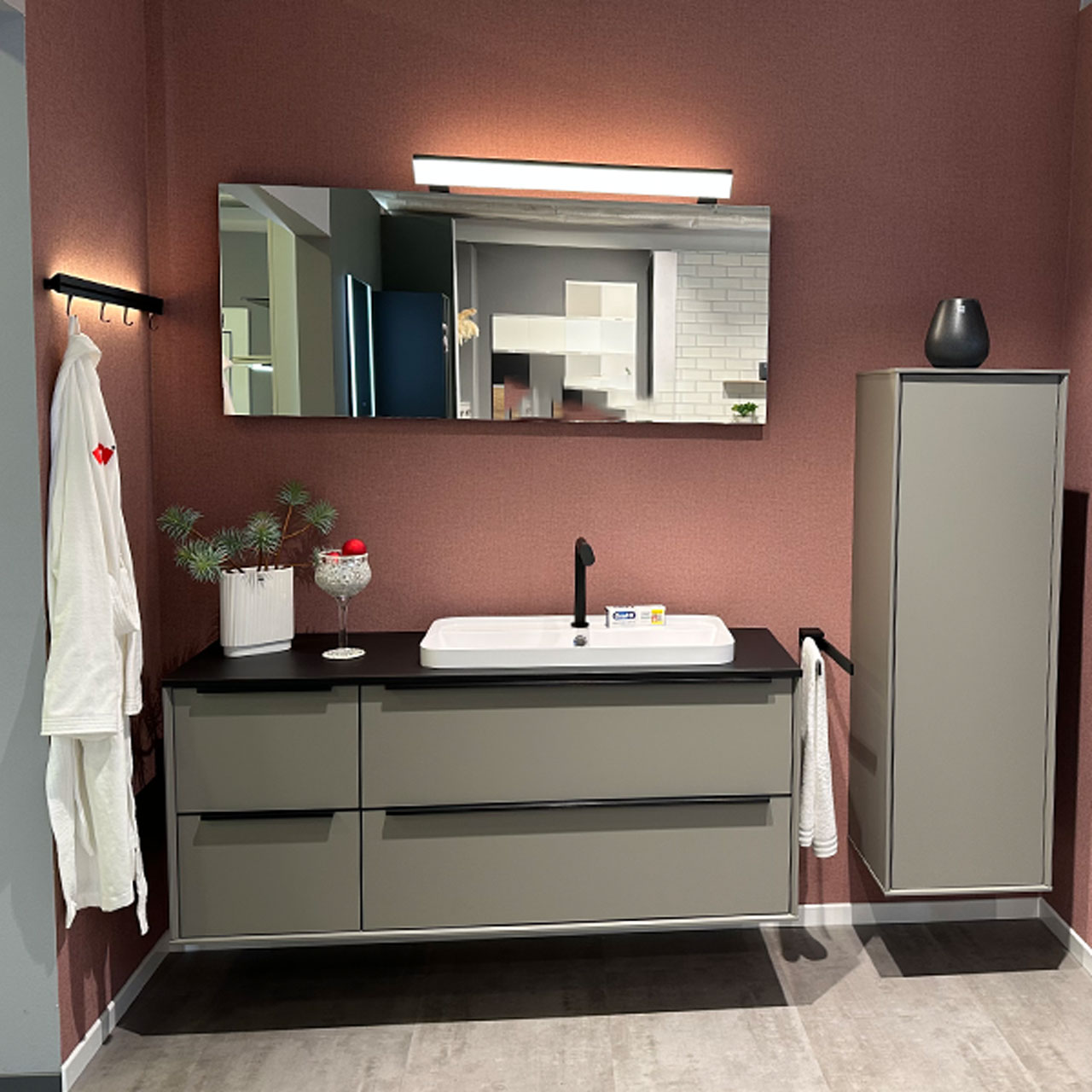 MH_Kachel_Ausstellungsbad Das Bild zeigt einen Aufbau aus der Badezimmerausstellung. Spiegelschrank, Waschtisch mit aufgesetztem Waschbecken, Schubladenunterschrank und Hängeelement in der Farbe Grau-Braun mit schwarzer Ablage und schwarze Griffen und Amatur.