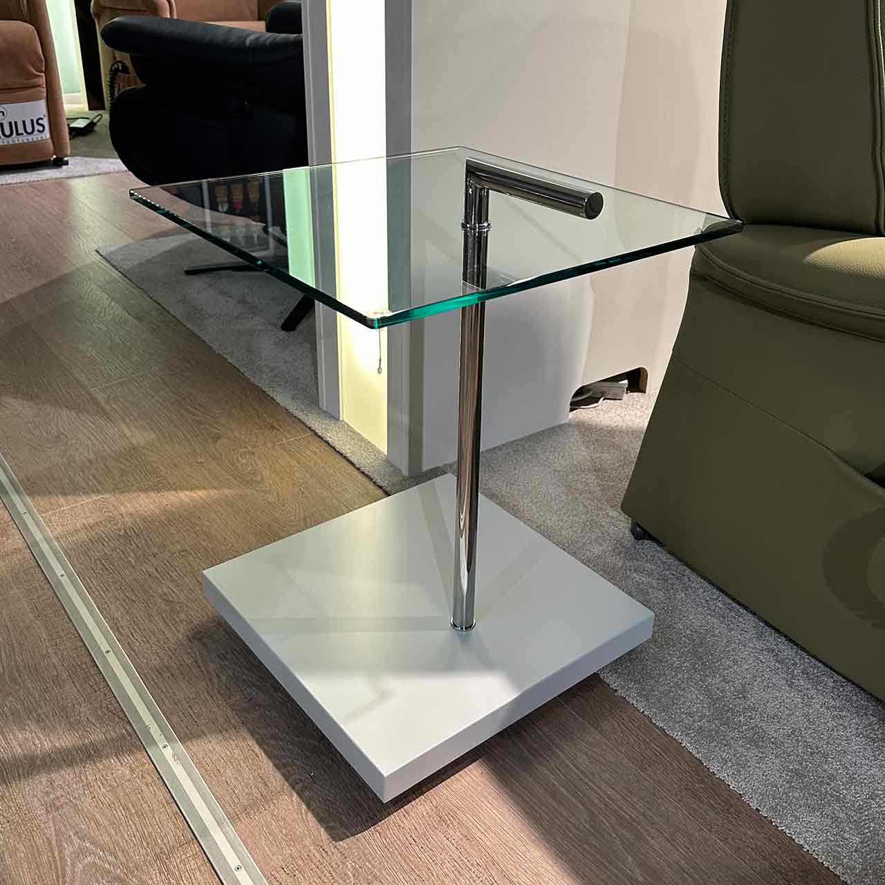 Beistelltisch mit quadratischer Glasplatte auf chromfarbiger Säule mit quadratischem weißem Sockel.