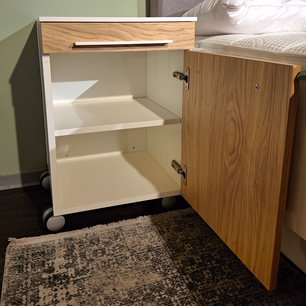 Loddenkemper - Bettanlage mit Konsolen Bettkonsole mit weißen Korpus und Fronten in Balkeneiche. Die Tür ist geöffnet.