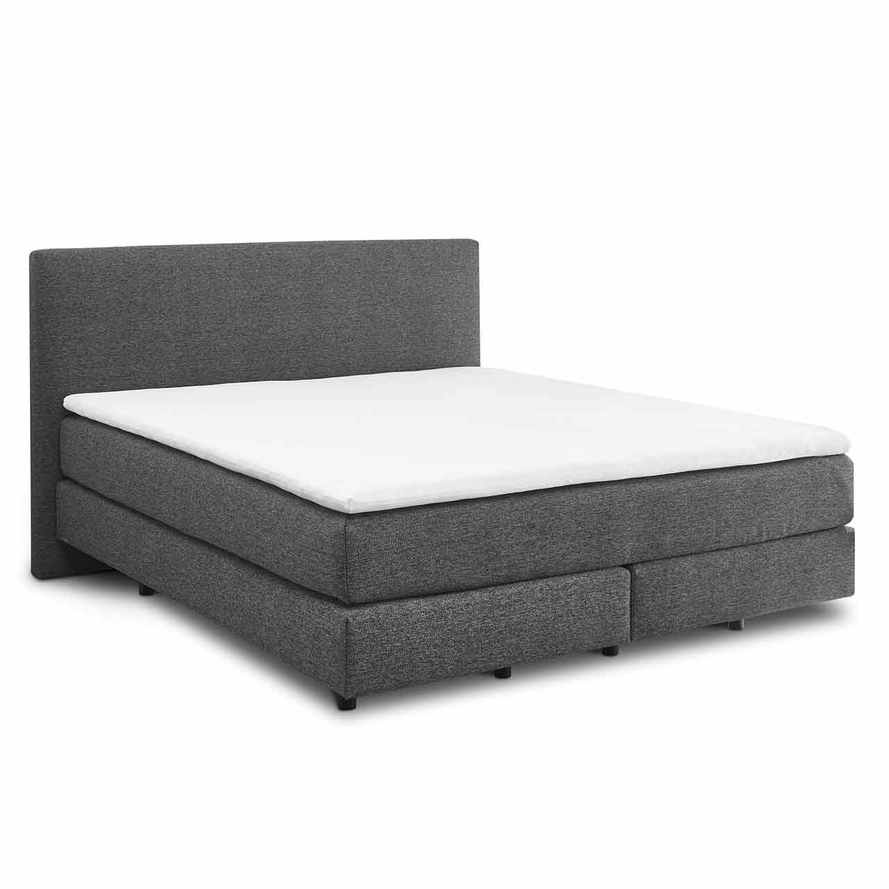 Hellgraues Boxspringbett mit zwei Boxen unten und darüber zwei Matratzen in einer Hülle. Darauf liegt ein weißer Topper. Das Kopfteil ist glatt mit dem gleichen Stoff bezogen.