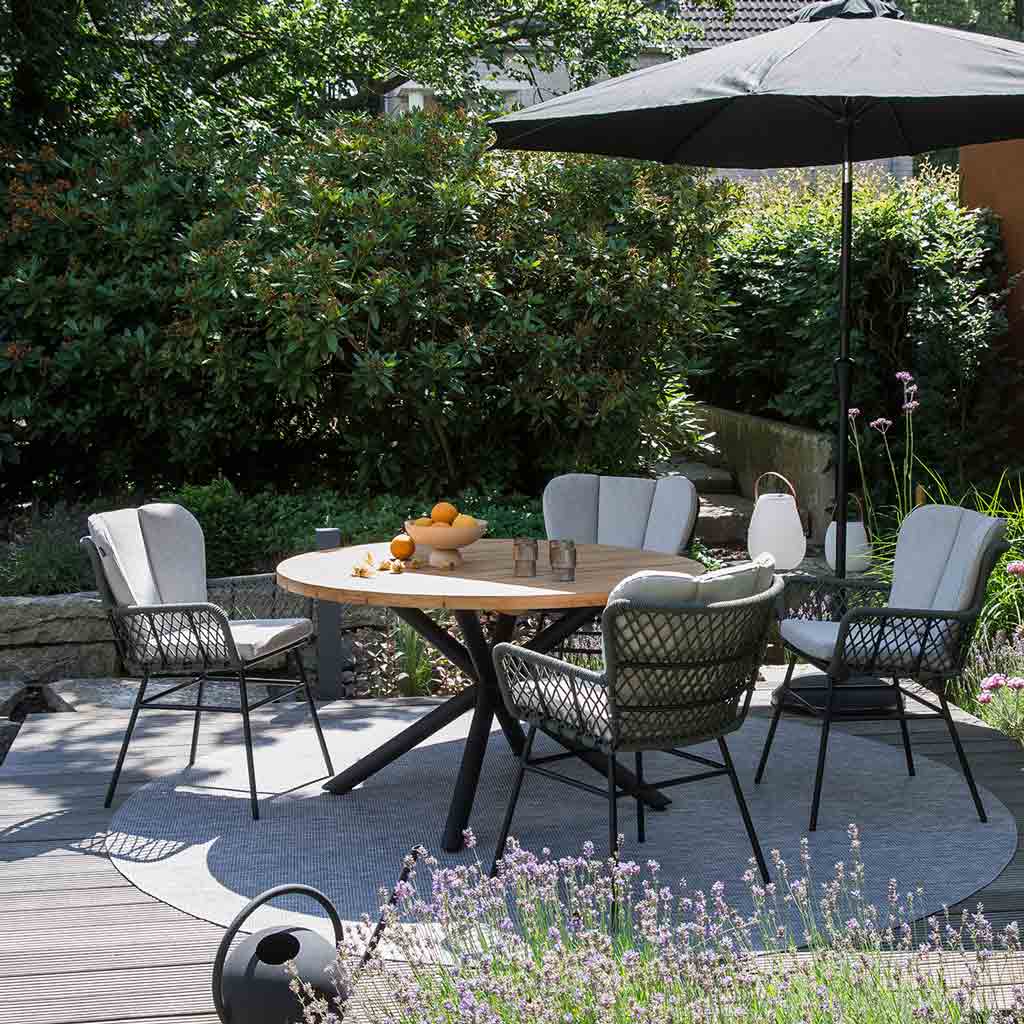 Gartenesstisch Kombination aus Geflecht Stuhl Bennett und Teakholztisch Saba. Runder Gartentisch SABA mit Teakholz Platte und Sternförmiges schwarzes Untergestell. Beistehend sind vier Bennett Geflecht Stühle inkl. Kissen.