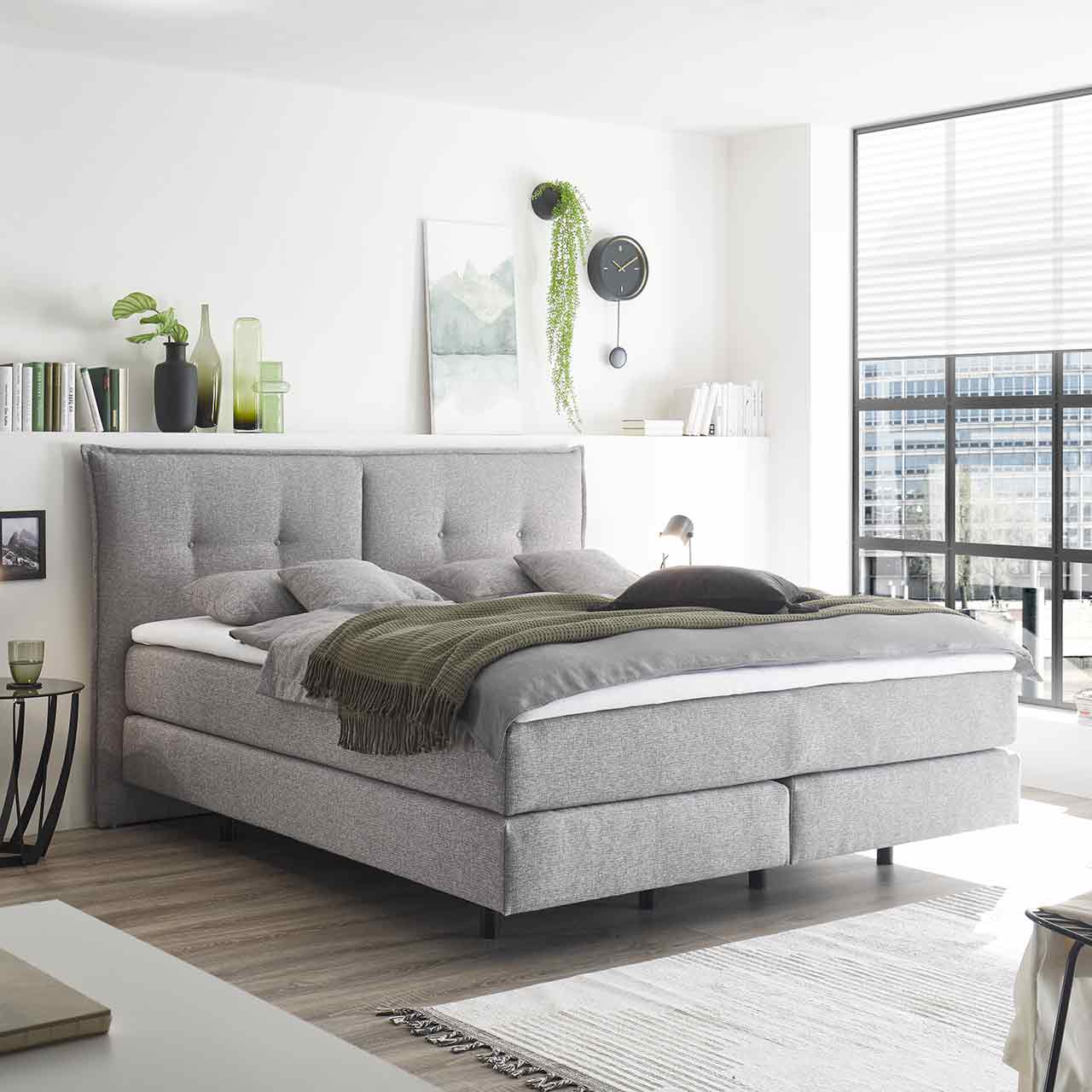 Gleiches Bett in einen Schlafzimmer mit viel Dekoration, Kissen und Decken.