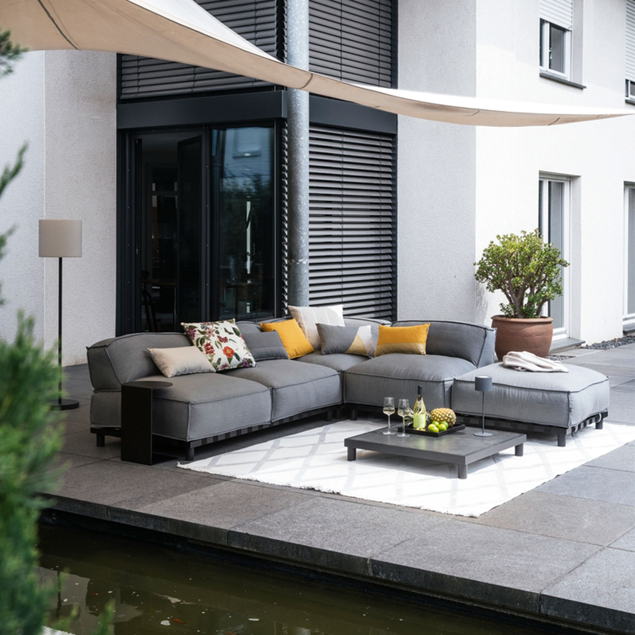Ambiente Bild der Gartenlounge Vlieland Hocker mit schwarzen Metalluntergestell und wetterbeständigen grauen Sunbrella Stoff.