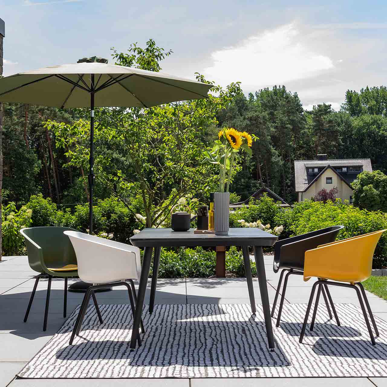 Gartenesstischgruppe Texel mit rechteckigen Esstisch mit schwarzer Glas-Keramik Tischplatte dabei stehen vier Kunstoffschalen Stühle der Serie in gelb, grün und Schwarz und weiß. 