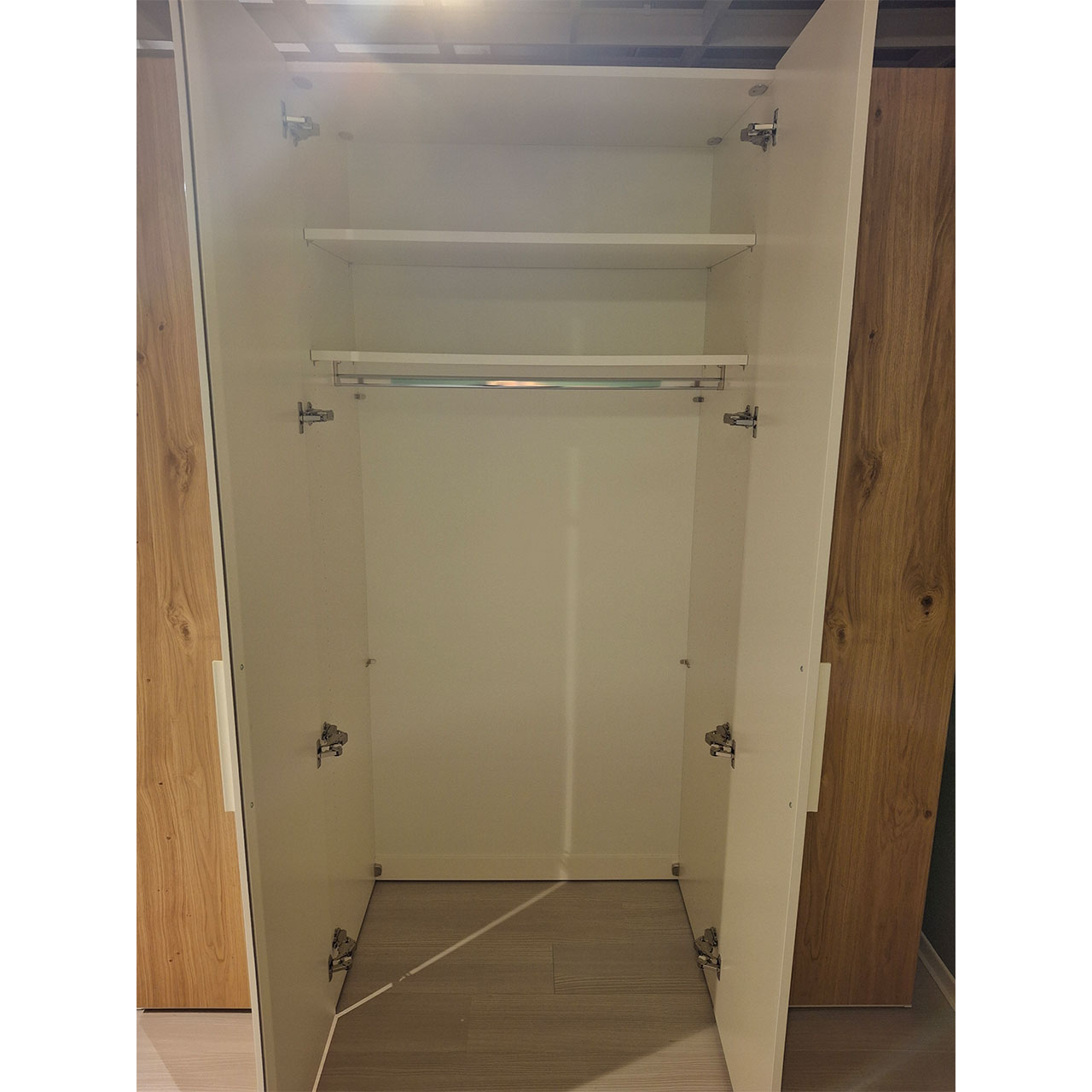Detailaufnahme Kleiderschrank. Die mittleren Türen sind geöffnet. Zu sehen sind eine Kleiderschrank und zwei Einlegeböden.