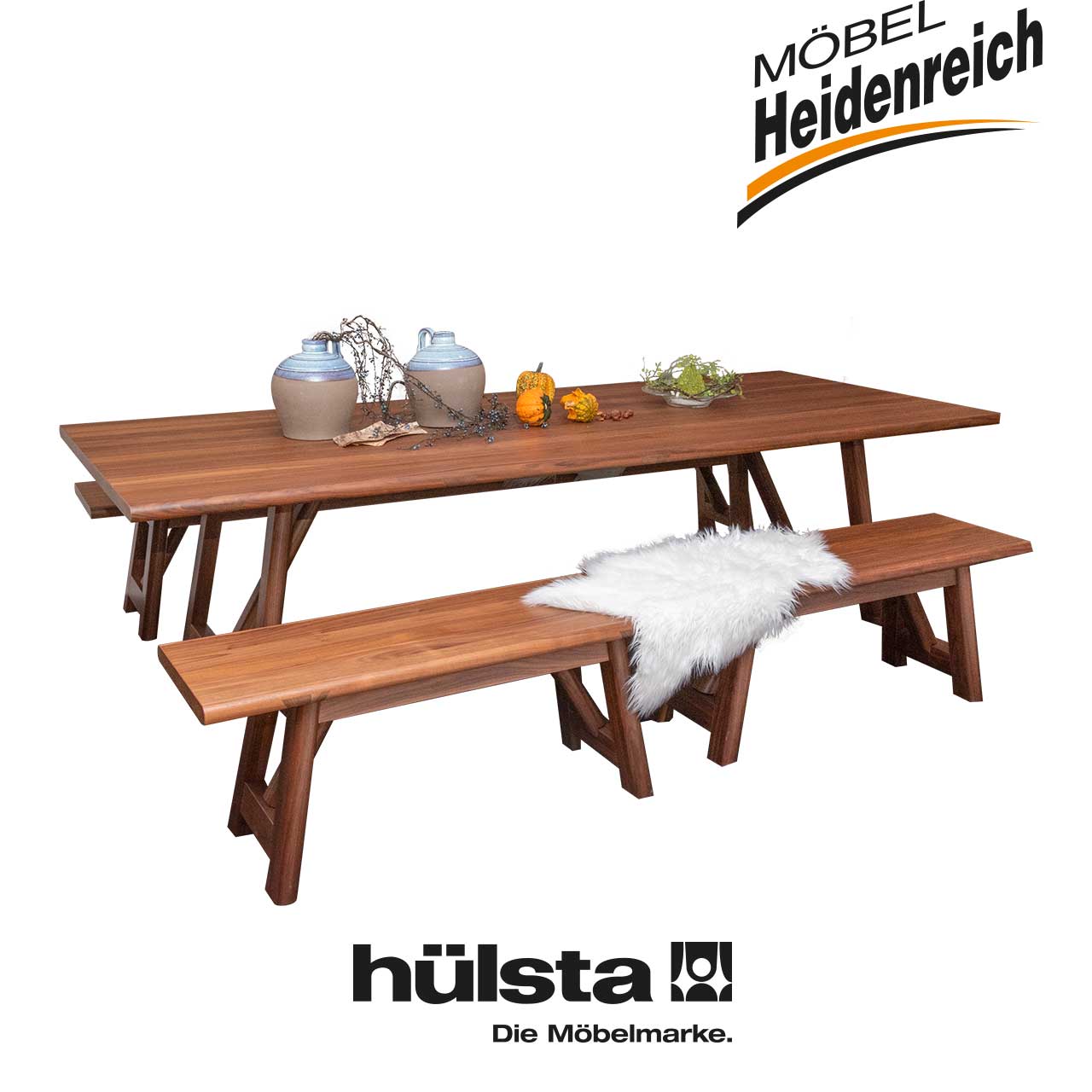 Tischgruppe aus dunklem Holz bestehend aus einem Tisch mit rechteckiger Tischplatte und drei Bänken ohne Lehne, eine lang, zwei kurz.