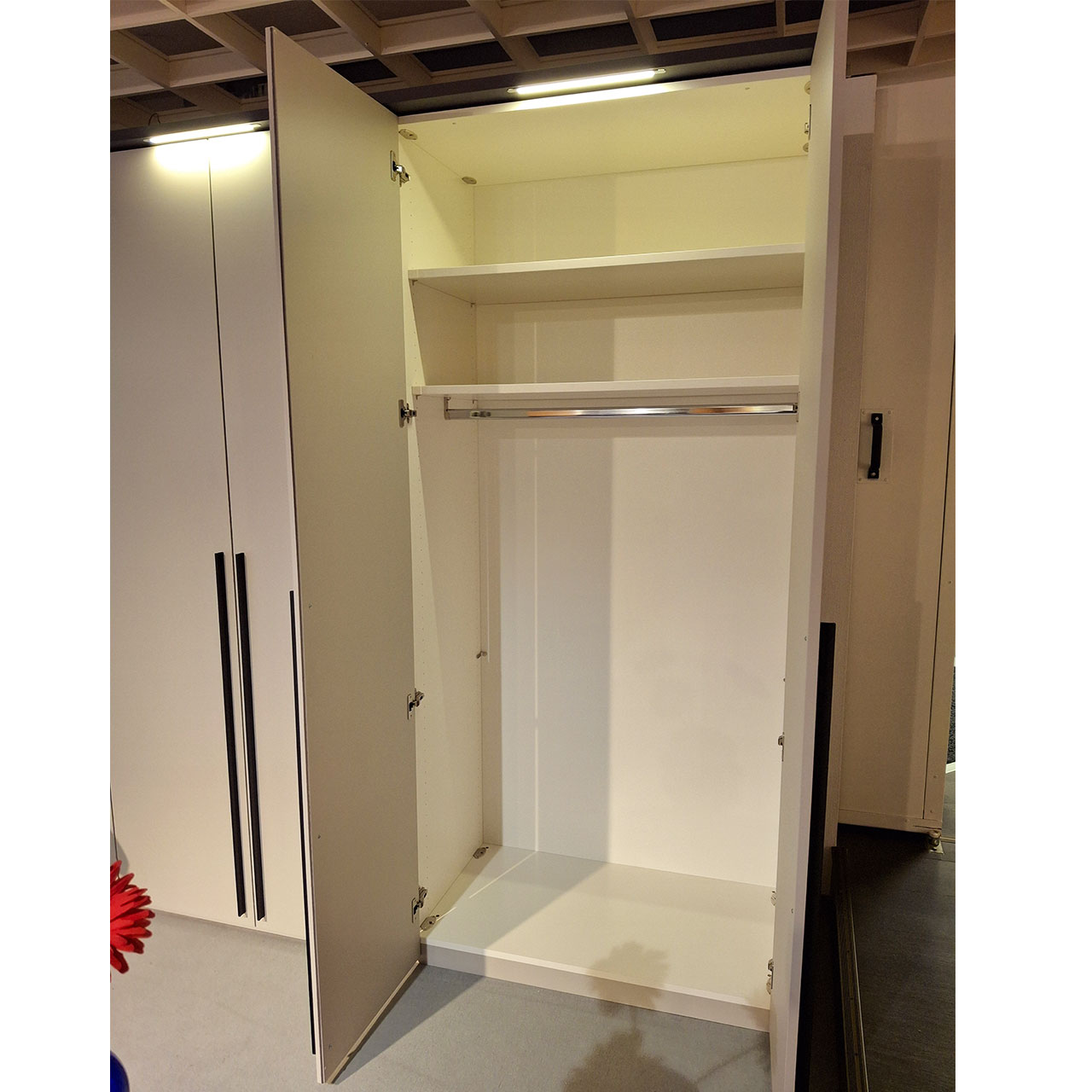 Mehrtüriger Kleiderschrank mit LED-Beleuchtung über jeder Doppeltür. Die Doppeltür ganz rechts ist geöffnet. zu erkennen sind eine Kleiderstange und zwei Einlegeböden im oberen Drittel des Schrankes.