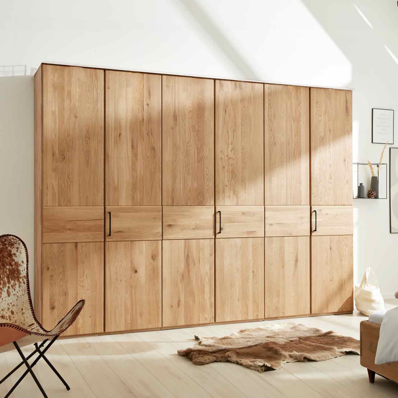 Kleiderschrank aus hellem Holz mit 6 Türen. In der Mitte eine durchlaufende optische Absetzung. An jeder zweiten Tür ist ein Griff.