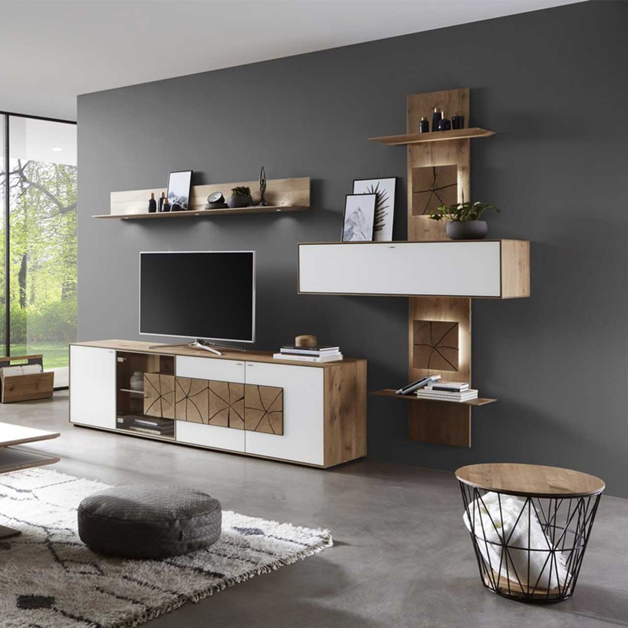 Stilvolle, moderne Wohnwand in weiß und Holz mit Spaltholzoptik und grauem Sitzpouf. 