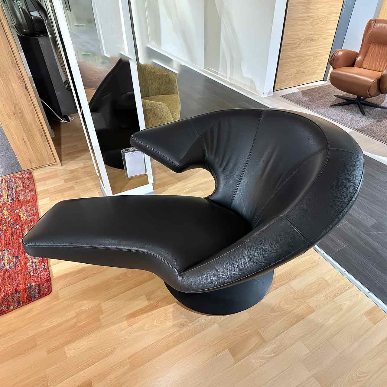 Drehsessel von der Seite: Auf der rechten Seite steht eine prominente Armlehne hervor, das Fußteil ist liegenartig fixiert.