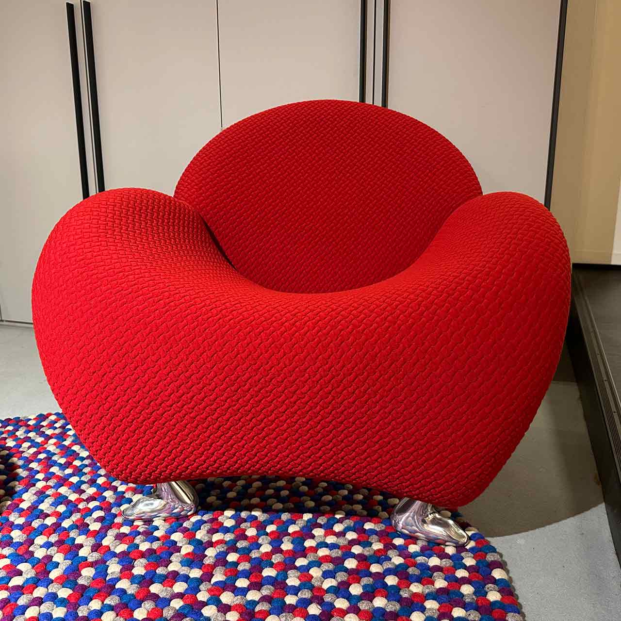 Rundlicher Sessel mit rotem Stoffbezug und tierisch anmutenden Füßen aus glänzendem Metall.