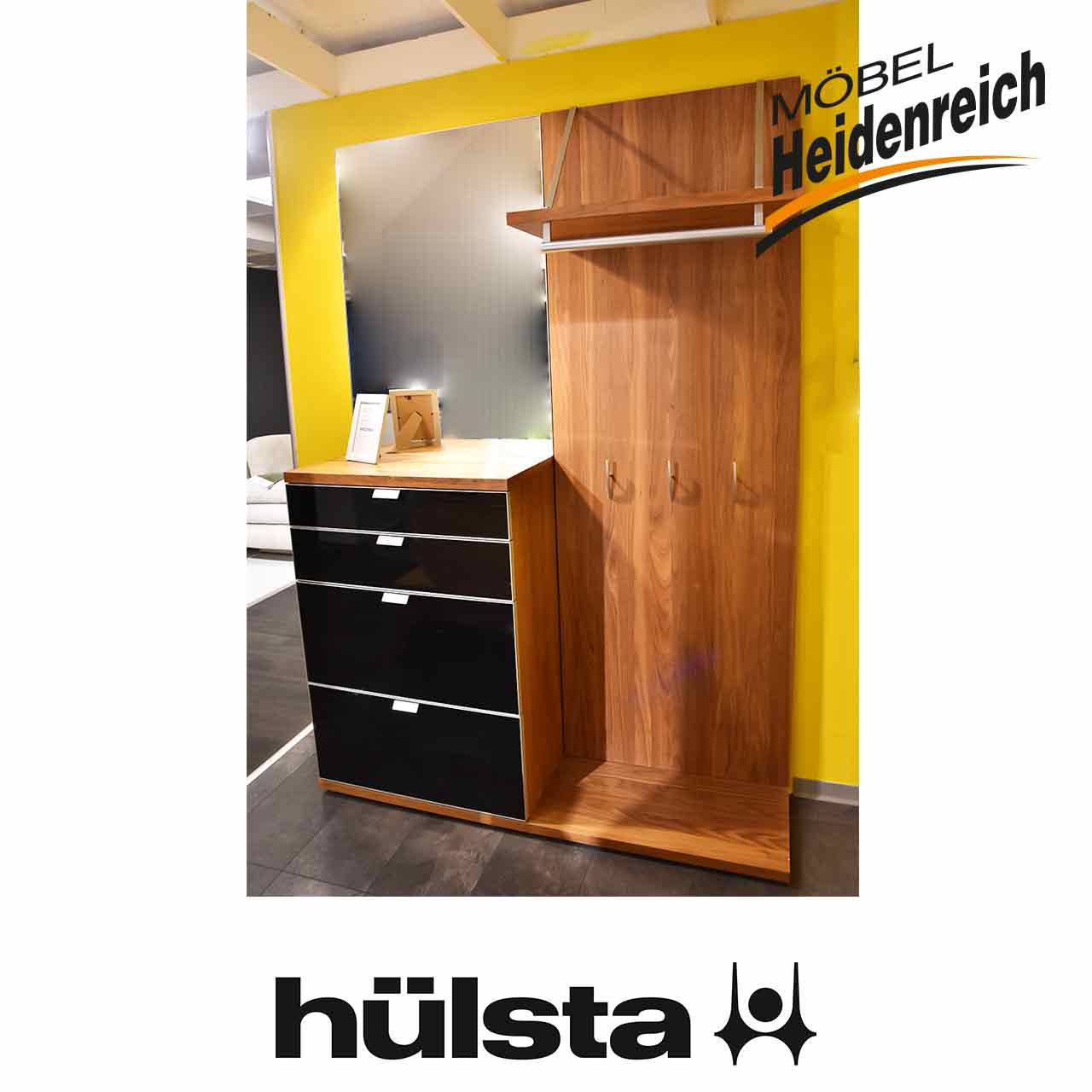 Links Spiegel und darunter Kommode aus dunklem Holz mit vier Schubladen mit schwarzer Front und Metallgriff. Daneben Garderobenpaneel aus dunklem Holz mit Hutablage und Kleiderhaken.