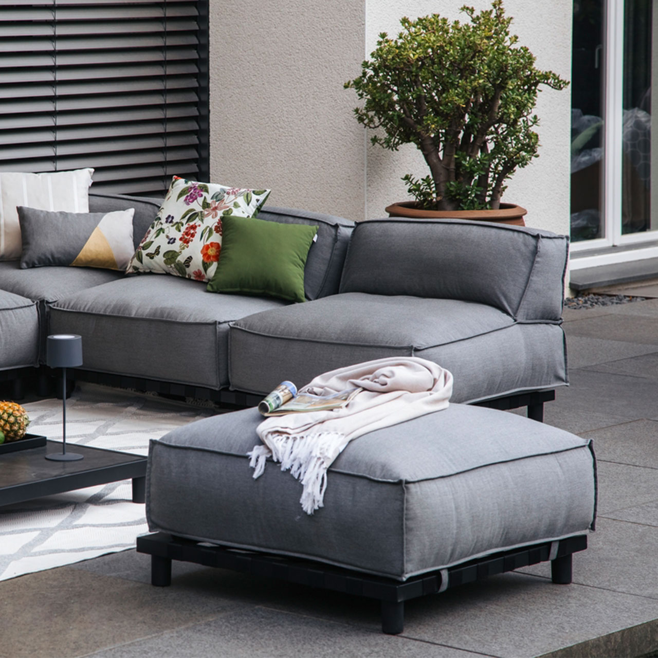 Ambiente Bild der Gartenlounge Vlieland Hocker mit schwarzen Metalluntergestell und wetterbeständigen grauen Sunbrella Stoff.
