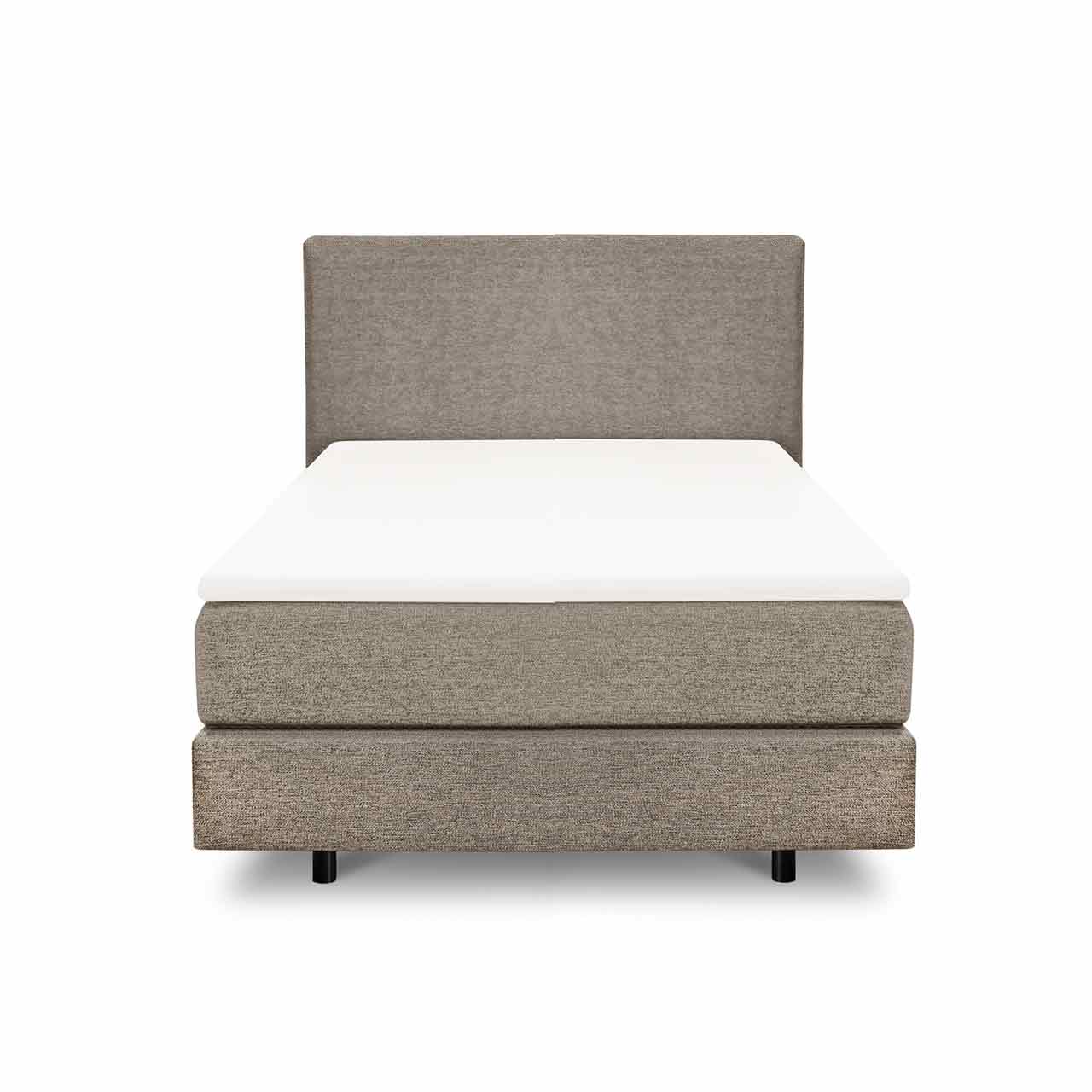 Schmales Boxspringbett in beigem Stoff mit einer Box unten und mit Möbelstoff bezogener Matratze darüber. On Top liegt ein weißer Topper. Das Kopfteil ist glatt mit dem gleichen Möbelstoff bezogen.