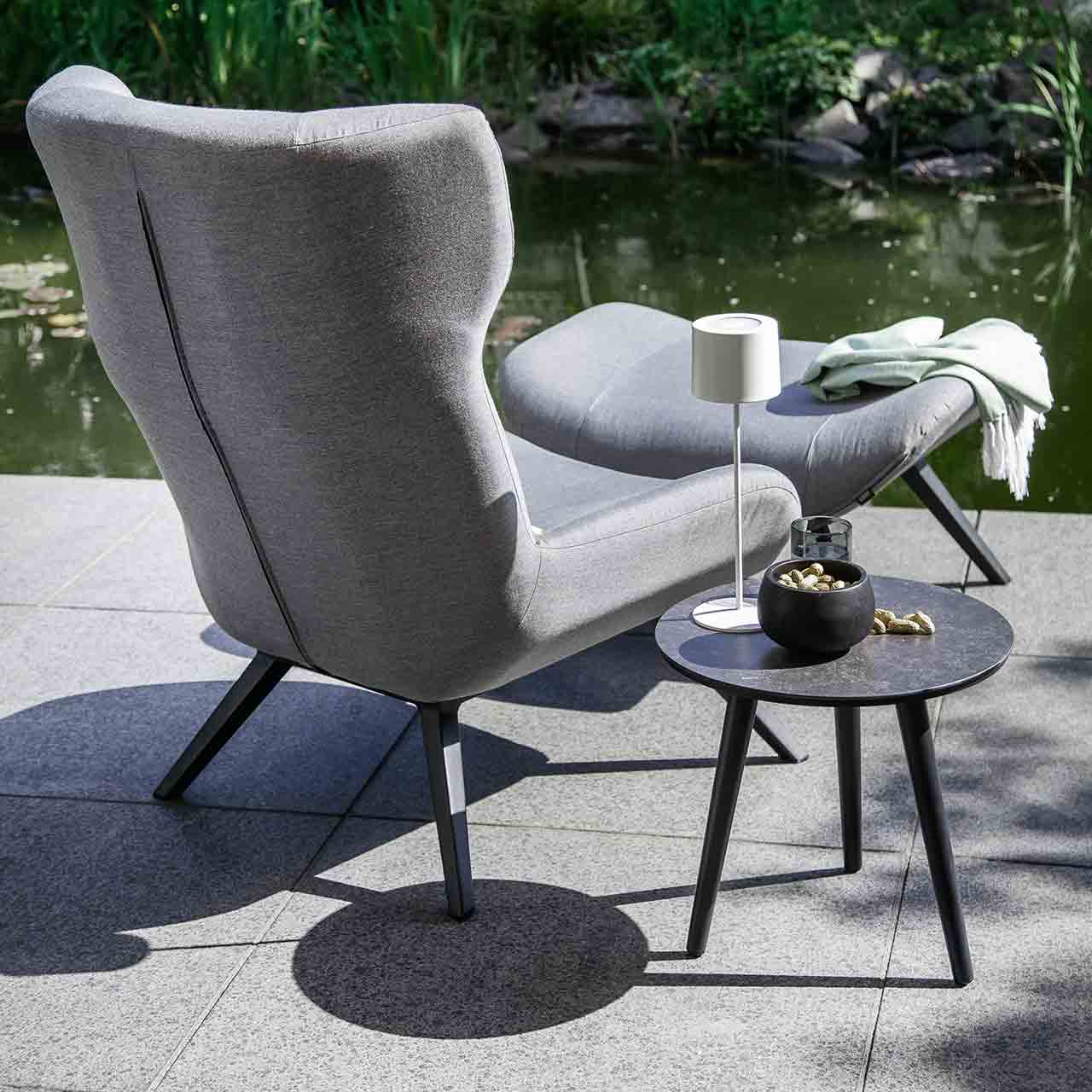 Schöner Wohnen - Rückenansicht vom Ohrensessel ELIN und Beistelltisch Texel Ohrensessel ELIN als Rückenansicht und der runder dreibeiniger Beistelltisch TEXEL mit schwarzer Glas-Keramik Tischoberfläche