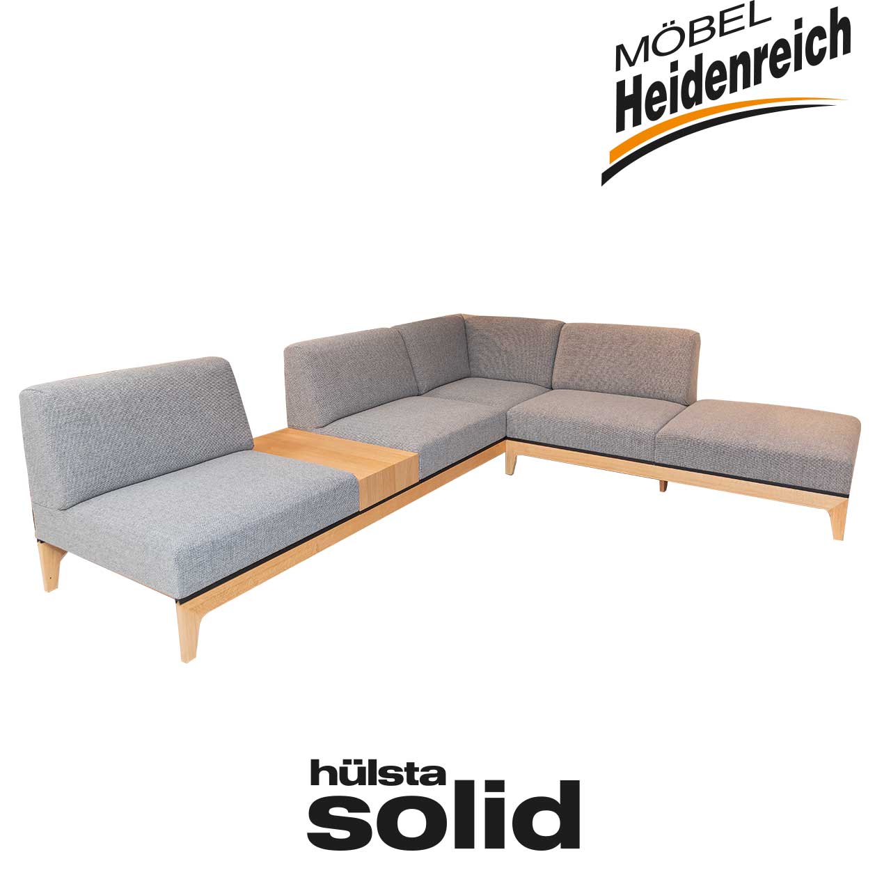 L-förmige Sitzecke aus grauem Stoff mit Füßen und Unterbau aus hellem Holz. Zwischen dem Sitzbereich links ein Einlegeboden aus gleichem Holz.