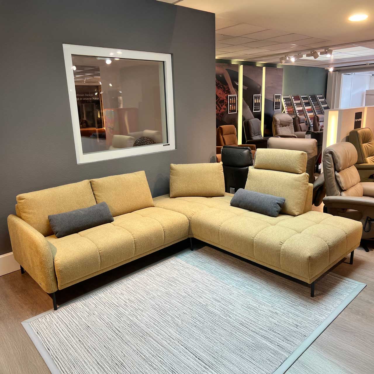 Ecksofa aus gelbem Stoff mit aufsteckbaren Kopfstützen und zwei grauen länglichen Kissen, die darauf liegen.