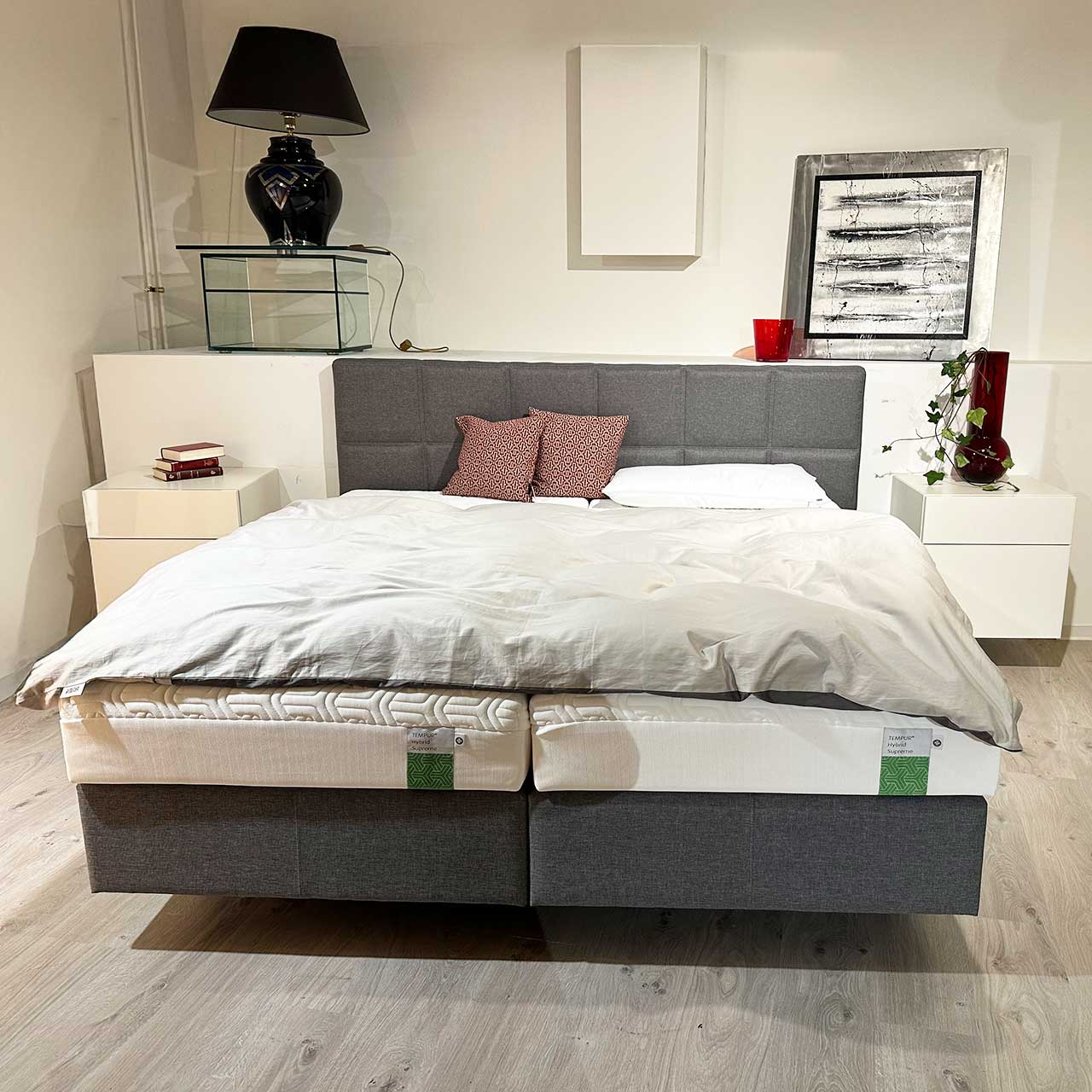 Boxspringbett aus grauem Stoff mit zwei Boxen, das Kopfteil ist in viele kleine Quadrate abgesteppt.