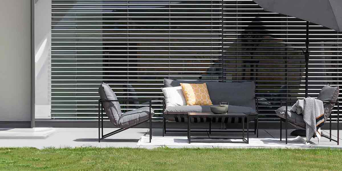 Gartenmöbel - zwei Sessel, Tisch und Bank mit Dekoration auf Terrasse vor einer heruntergelassenen Jalousie