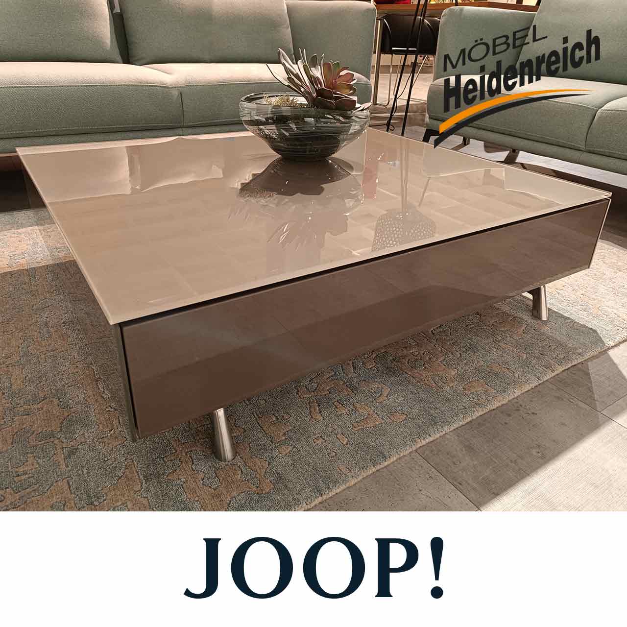 Hochglänzender brauner Couchtisch mit Glasplatte auf Stauraumfach sitzt auf vier metallfarbenen Beinen.