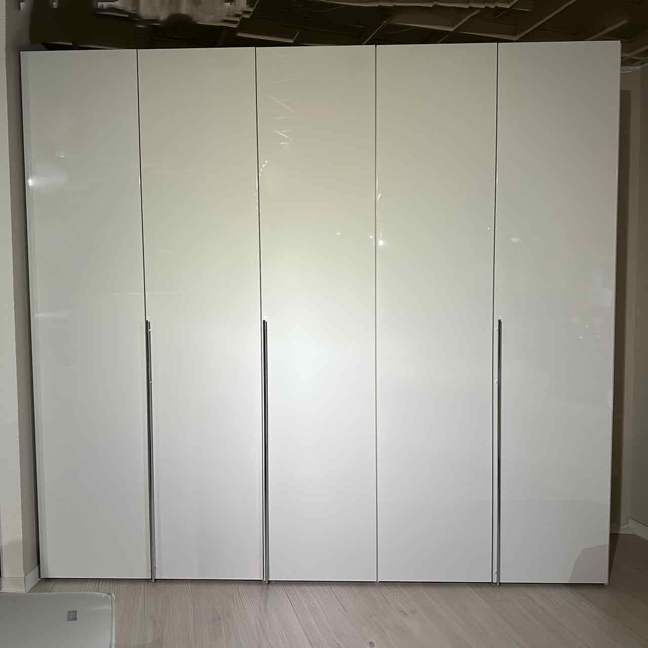 Weißer Kleiderschrank mit 5 Türen und drei langen Griffstangen, die vertikal montiert sind.