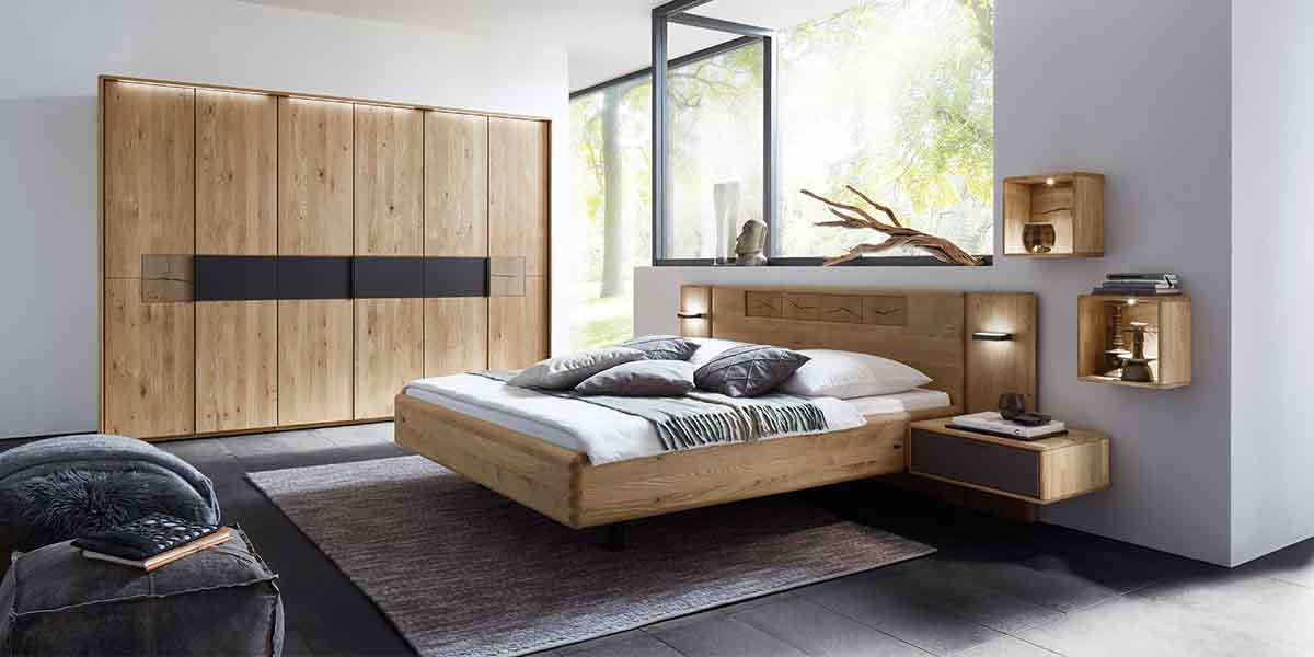 MH_Kategorie_Schlafzimmer Ambientebild Schlafzimmer mit integriertem Einbauschrank aus Holz mit anthrazitfarbenen Akzenten, passender Schlaflandschaft aus Holz mit integrierten Nachttischen und passenden Hängeelementen.