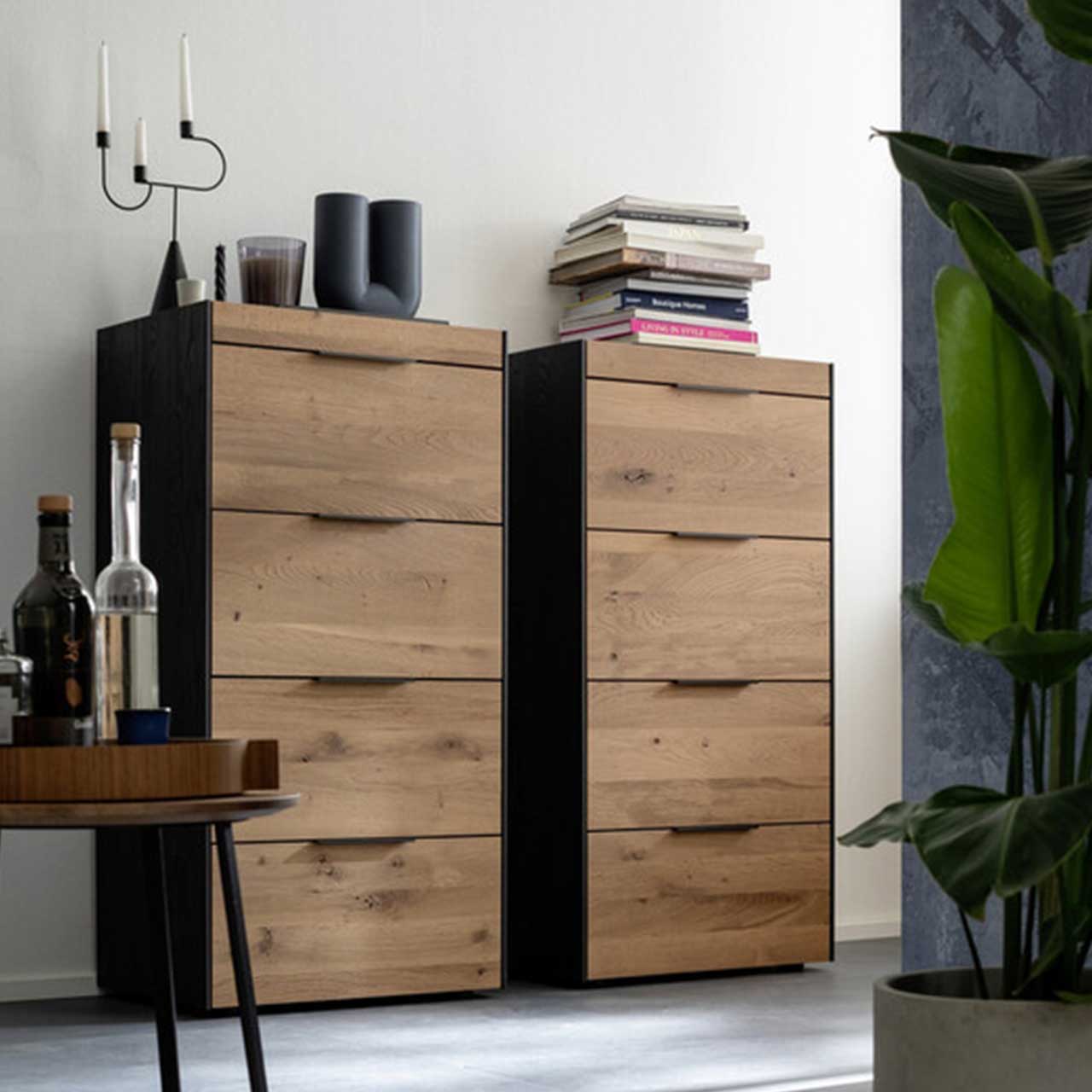 MH_Wohnzimmer_Highboards Amientebild mit zwei Highboards mit schwarzen Seitenwänden und Holzfront und dekorativen Elementen.