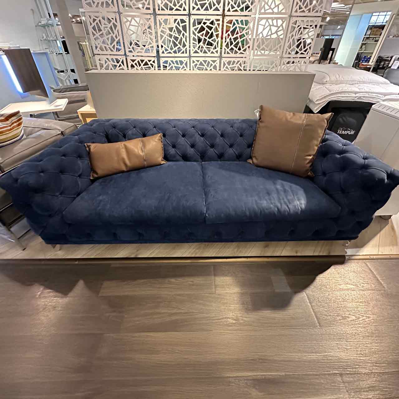 Blaues Nubuk-Sofa, Armlehnen gleiche Höhe wie Rückenlehnen, Rautenmuster in Lehnen gesteppt. Zwei braune Lederkissen liegen darauf.