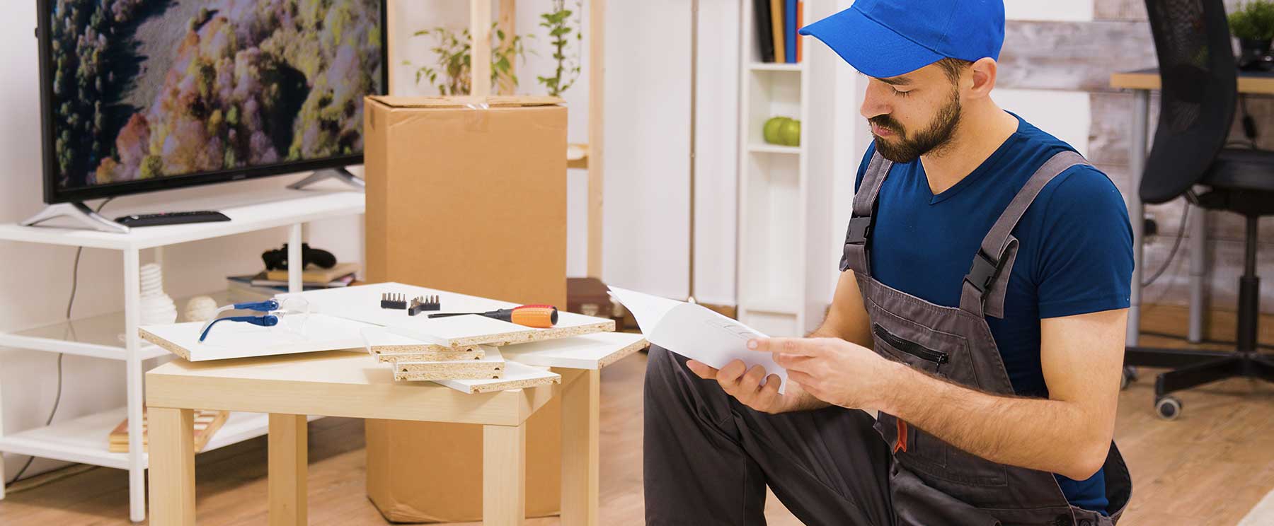 Ein Mann in Arbeitskleidung schaut gerade in die Montageanleitung für Möbel