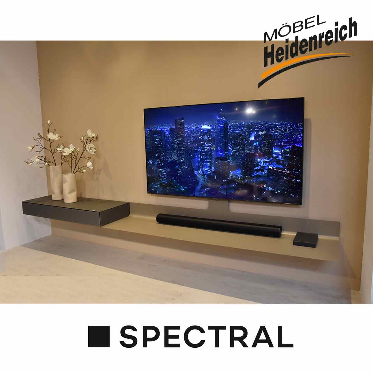 Schmale lange hellgraue Ablage mit links einer dunkelgrauen Kästchen mit Klappe. Daran montiert ein großer Fernseher.Auf der Ablage liegt ein Sonos-Gerät.