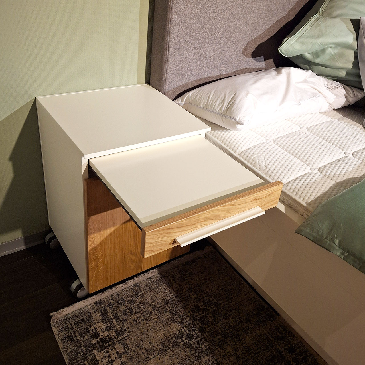 Loddenkemper - Bettanlage mit Konsolen Bettkonsole mit weißen Korpus und Fronten in Balkeneiche. Die Griffe sind weiß und ein Tablar ist ausgezogen.