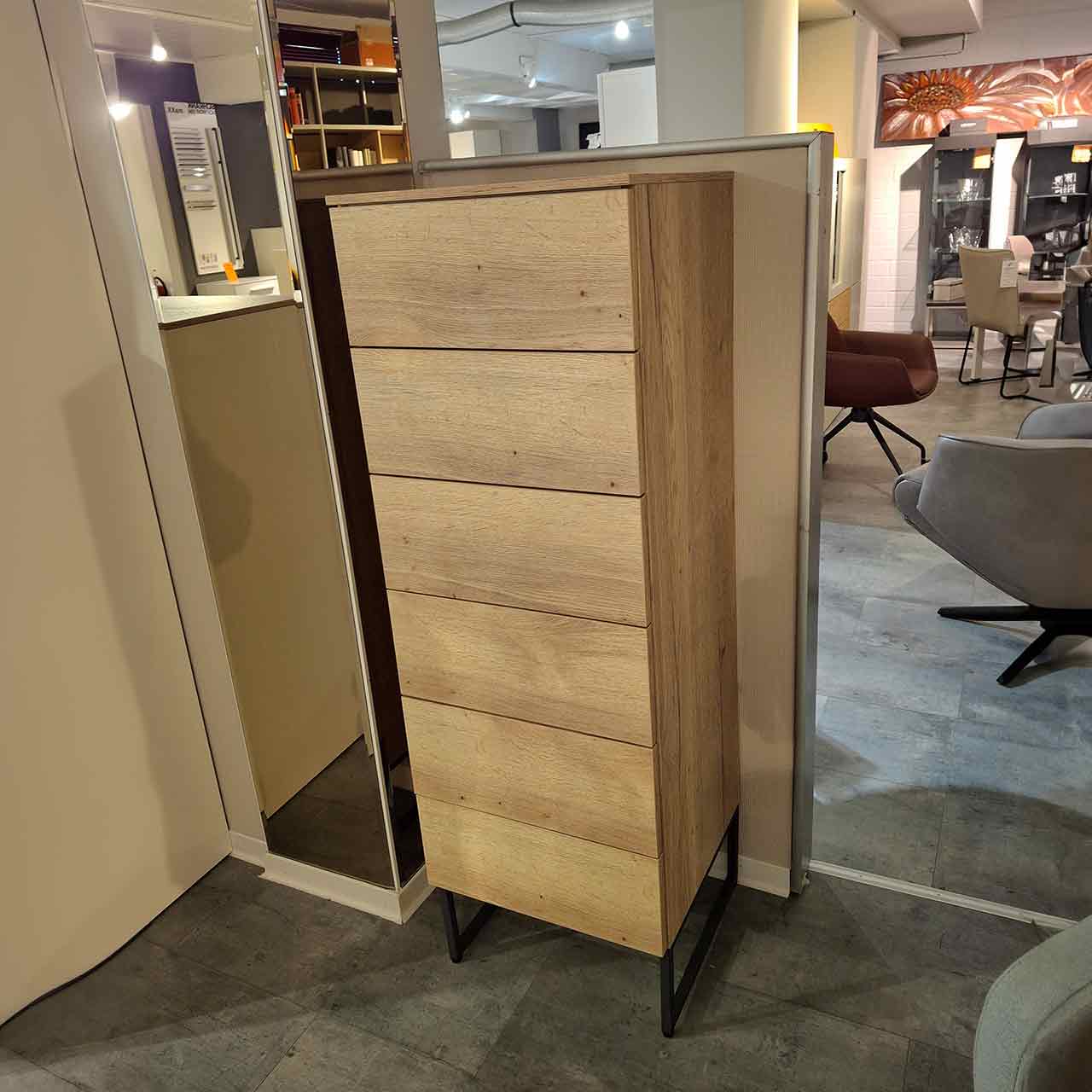 Loddenkemper Kommode maxx 600 Balkeneiche Hohe schmale Kommode aus heller Eiche mit sechs grifflosen Schubkästen. Steht auf zwei grauen Kufen.