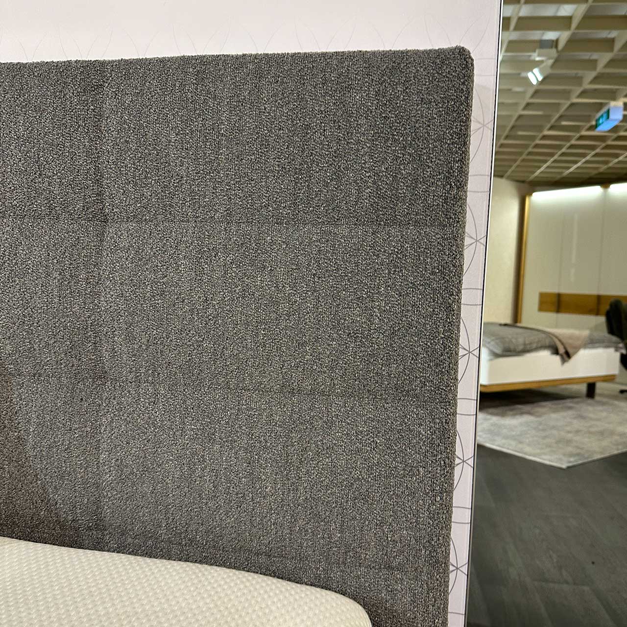 Detailansicht des Kopfteils. Das mit grauem Stoff bezogene Kopfteil ist mittels Ziernähten optisch in zahlreiche Quadrate aufgeteilt.