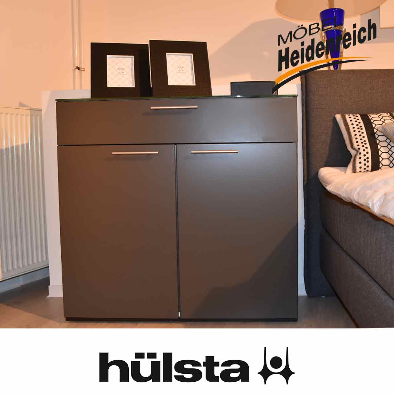 Hülsta Multi-Varis - Kommode grau Graue Kommode mit grauer Glas-Abdeckplatte. Oben eine Schublade, unten zwei Türen mit silbermatten Griffen.
