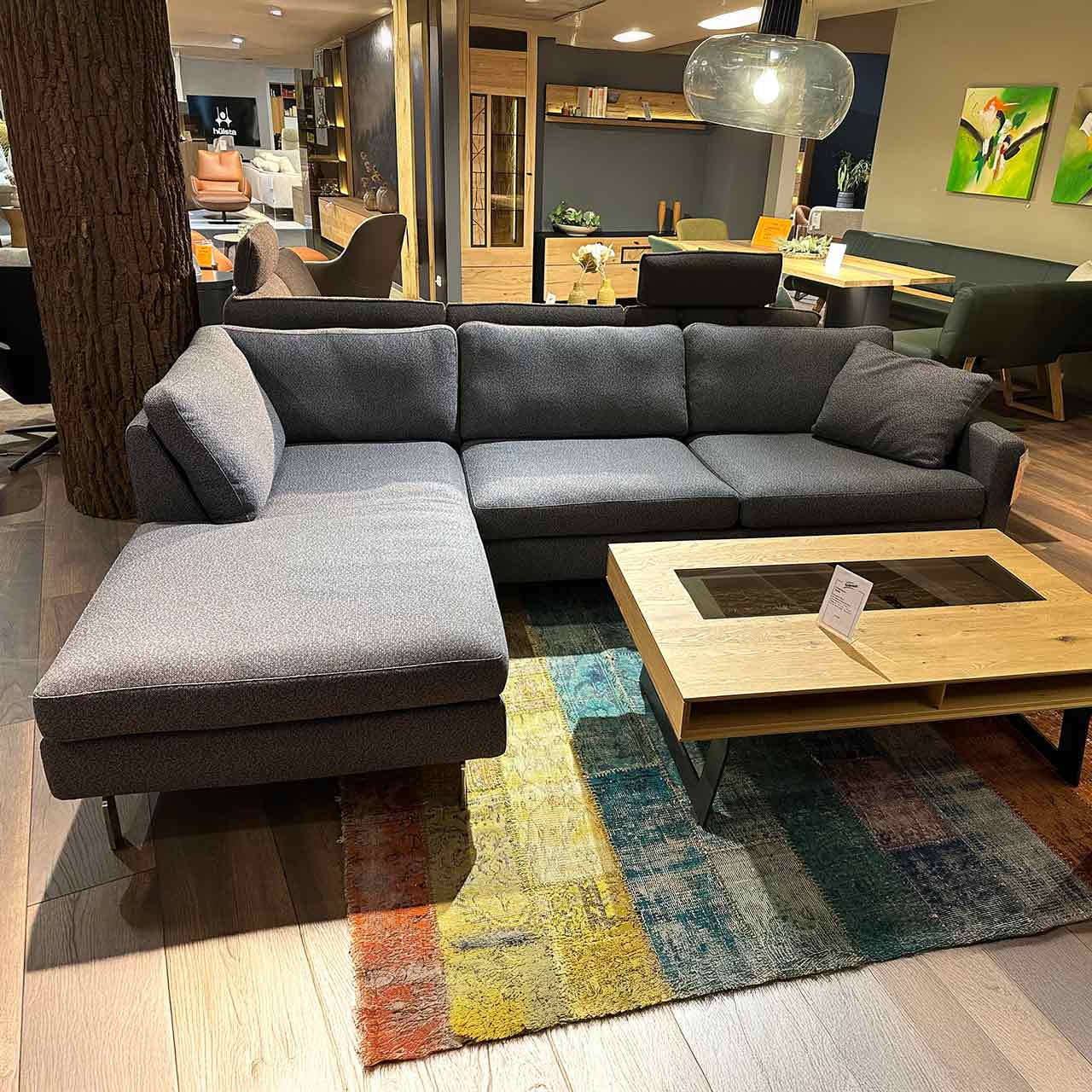 Graues Sofa mit Longchair links, zwei Sitzplätze rechts und zusätzliches Deko-Kissen.