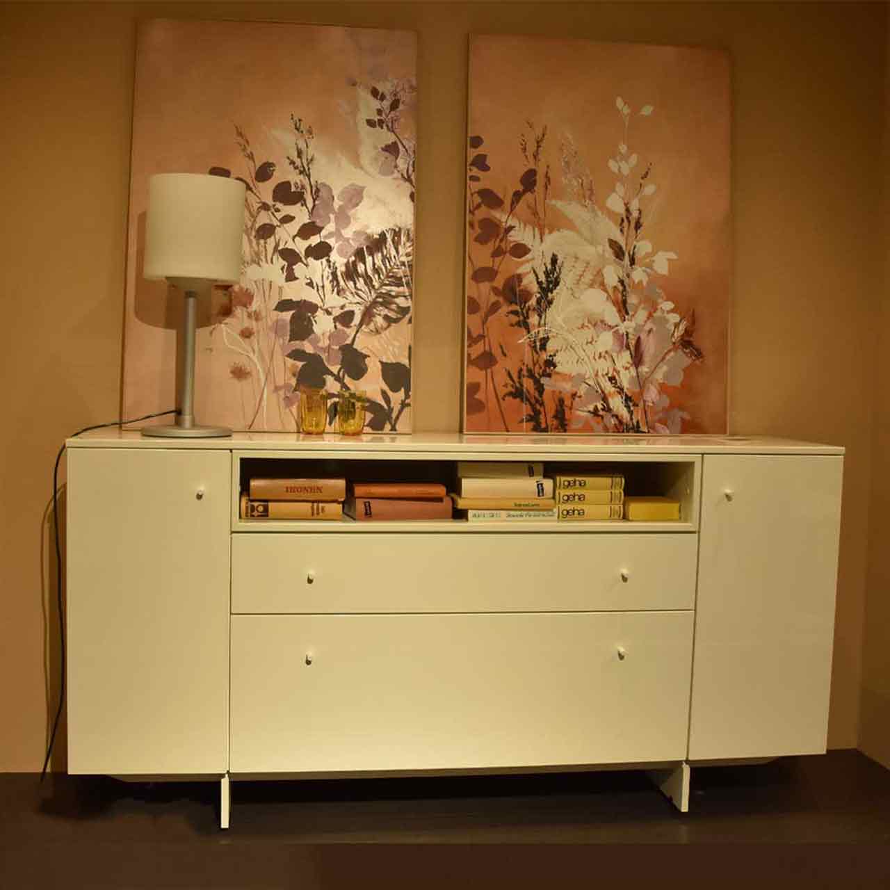 Weißes Sideboard auf Kufengestell mit Türen rechts und links und 1 Klappe und Schublade in der Mitte mit Dekoration in der Ausstellung