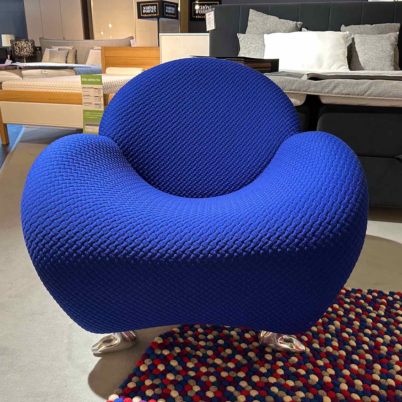 Rundlicher Sessel mit blauem Stoffbezug und tierisch anmutenden Füßen aus glänzendem Metall.