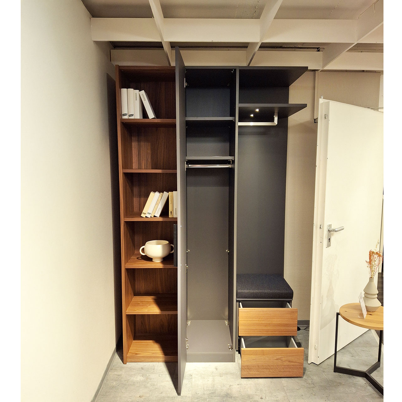 3-teiliger Garderobenschrank mit offenem Regal in Kernnussbaum links, mittig Regalschrank mit Tür in grau und rechts mit Anstellregal mit Beleuchtung und Sitztruhe unten.