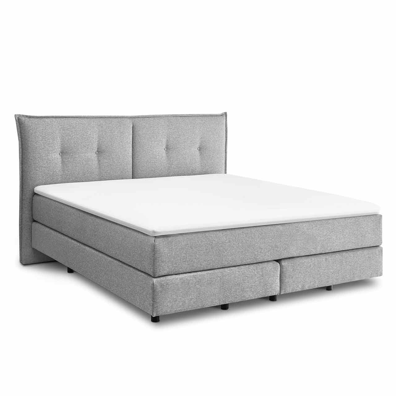 Hellgraues Boxspringbett mit zwei Boxen unten und darüber zwei Matratzen in einer Hülle. Darauf liegt ein weißer Topper. Das Kopfteil in Kissenoptik ist zweigeteilt und hat jeweils zwei Einzüge auf jeder Seite.