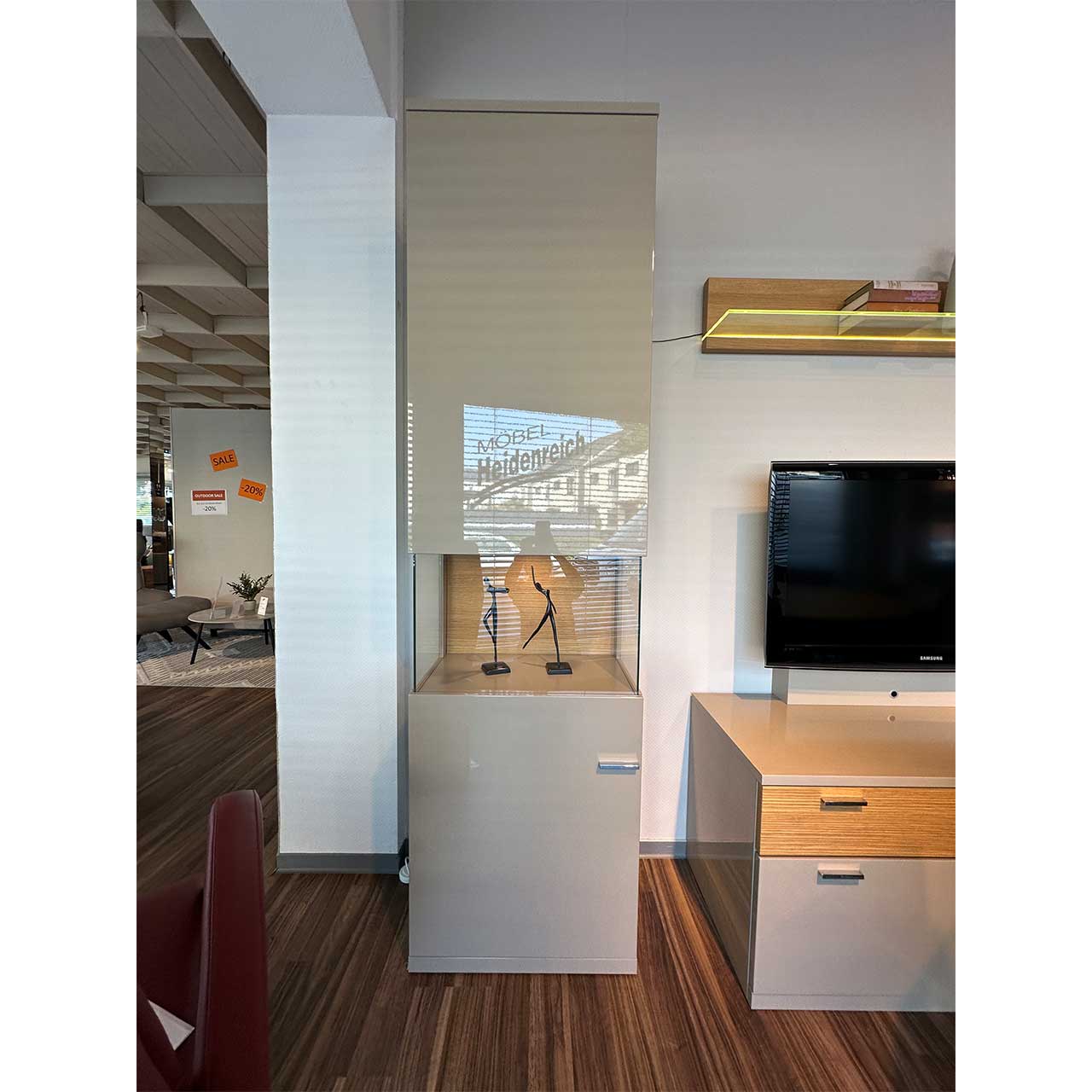 Die Hochglanz-Vitrine hat in der Mitte einen Glasausschnitt mit einer Rückwand aus hellem Holz.