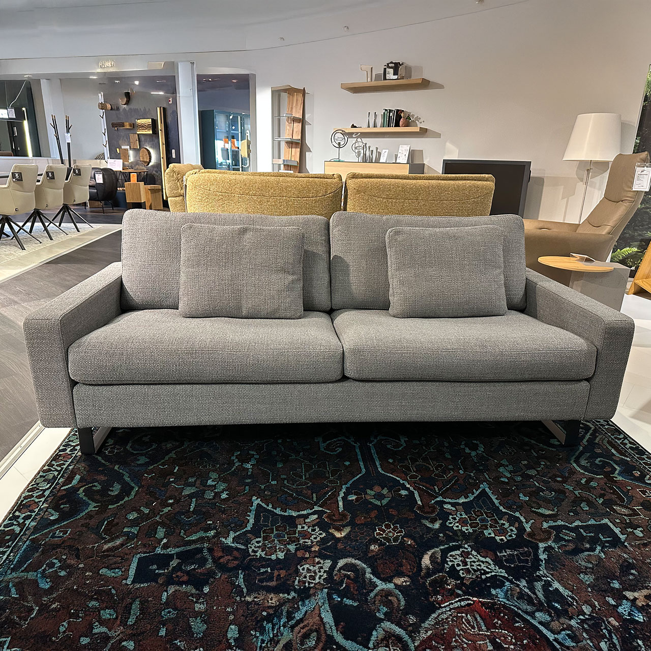 Zweisitzer mit niedriger Armlehne und zwei Kissen im gleichen grauen Stoff wie der Bezug.