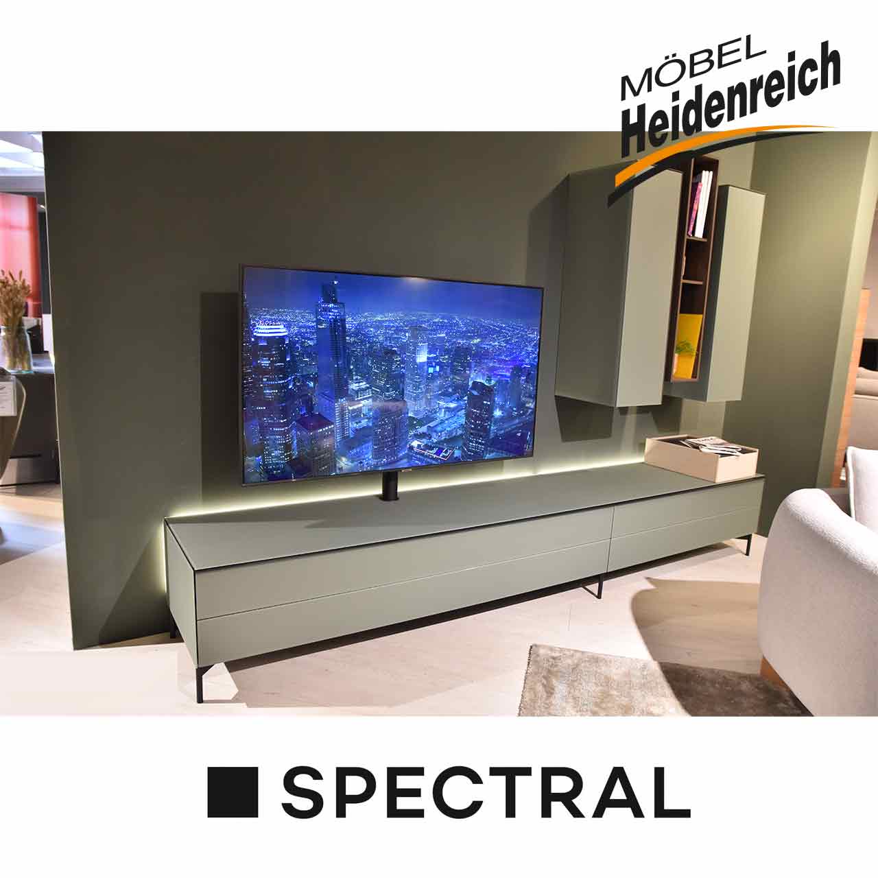 Spectral - Wohnwand Scala Wohnwand in Salbei-Farbe, Lowboard mit Klappe und Schubladen auf schwarzem Gestell, rechts oben zwei Hängeelemente mit Tür, die durch ein Hängeregal dazwischen aufgelockert werden.