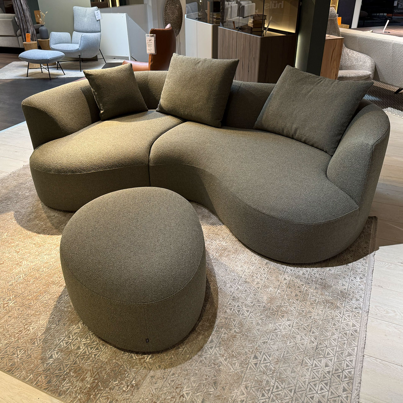 Organisch geformtes Sofa mit drei Kissen und organischem Hocker davor