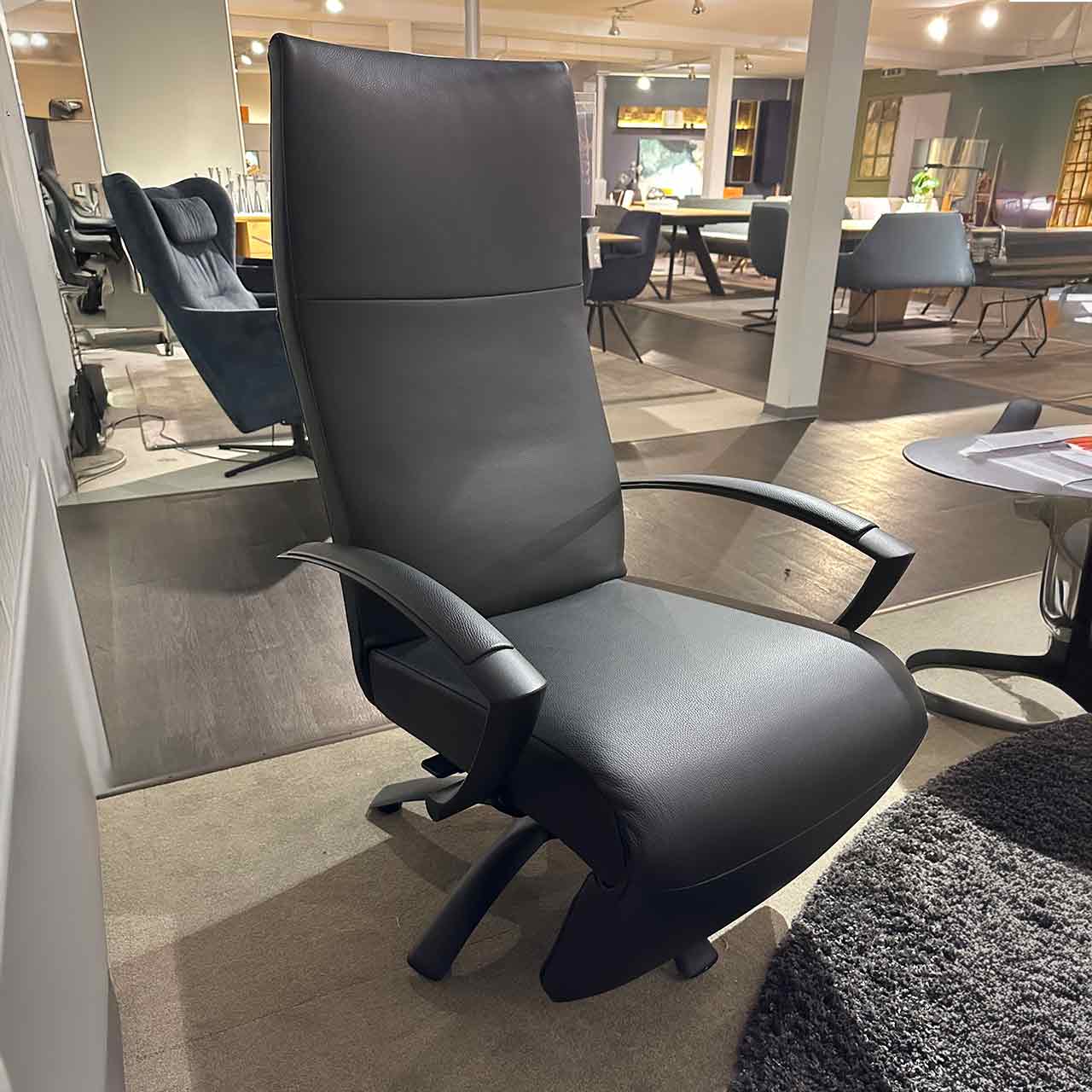 Relaxsessel aus schwarzem glatten Leder mit hohem Kopfteil und eingeklapptem Fußteil.